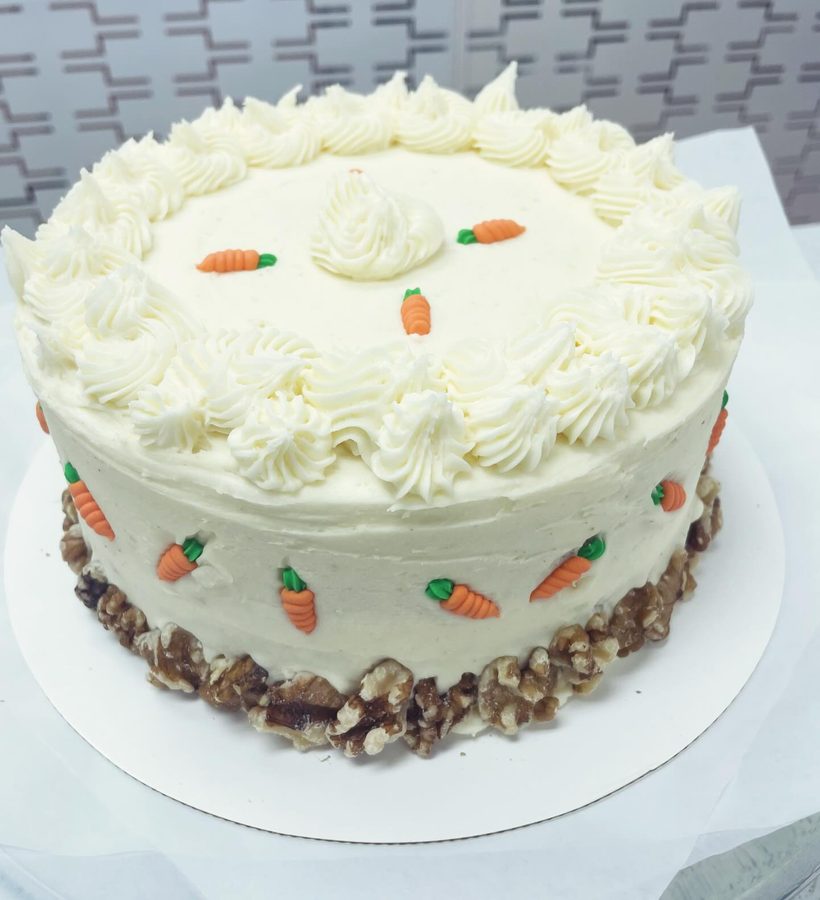 Carrot cake with white piped frosting, candy carrots and walnut-crusted sides from the bakery's Instagram